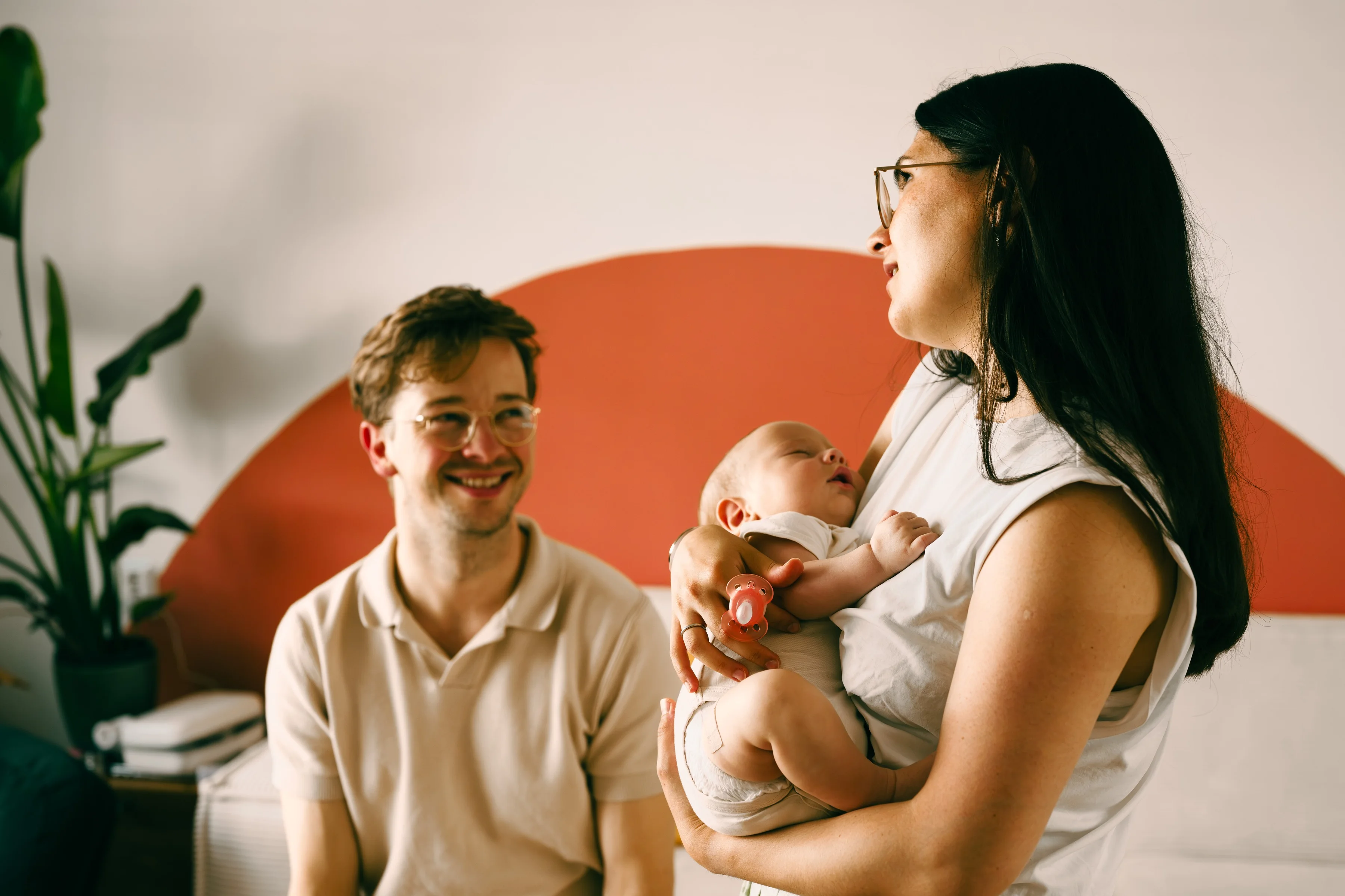 Parents sitting with their baby in front of an orange wall
