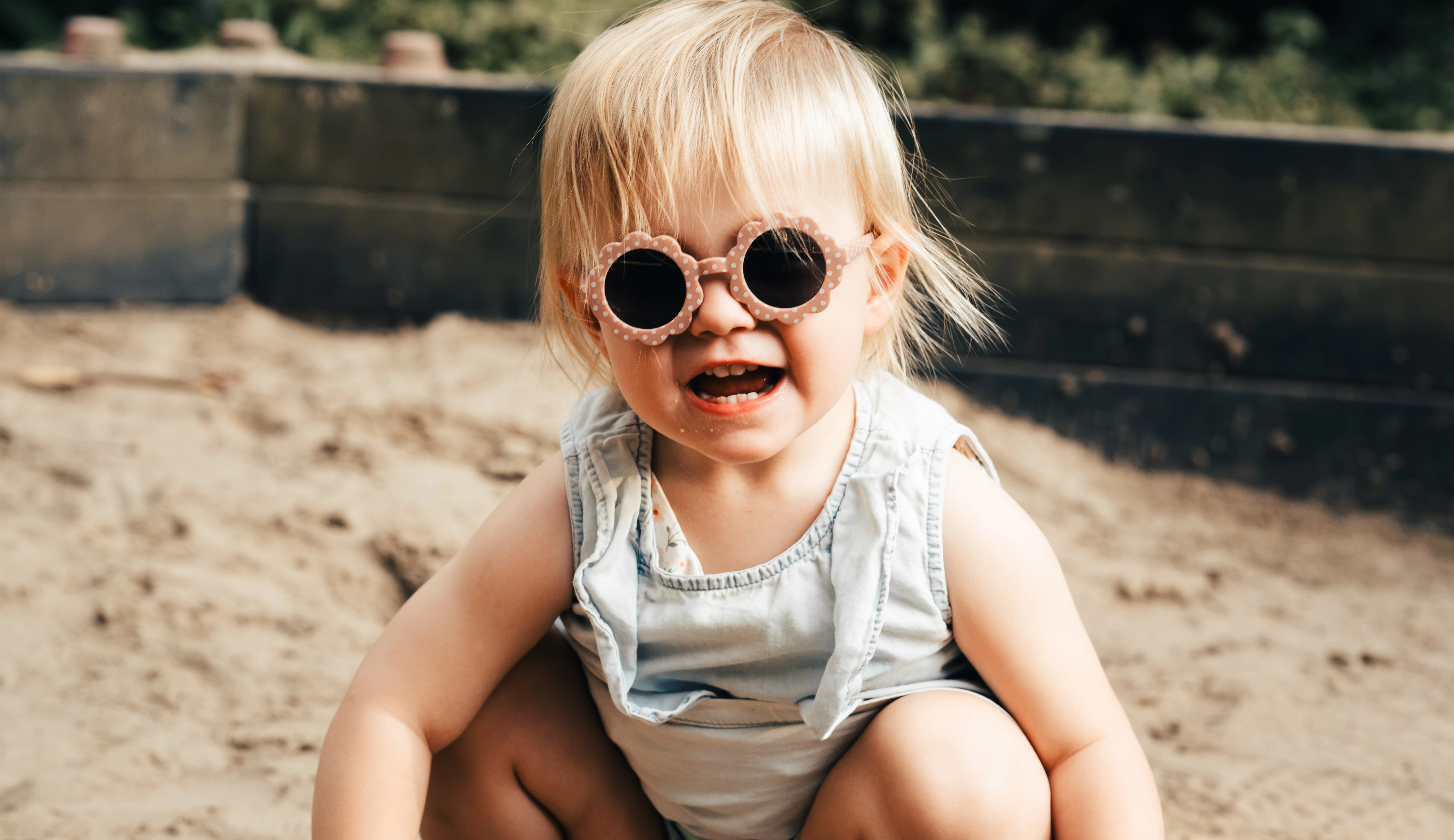 A toddler in sunglasses in a sandpit